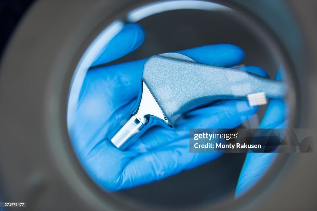 Engineer inspecting artificial hip joint through magnifier in orthopaedic factory, close up