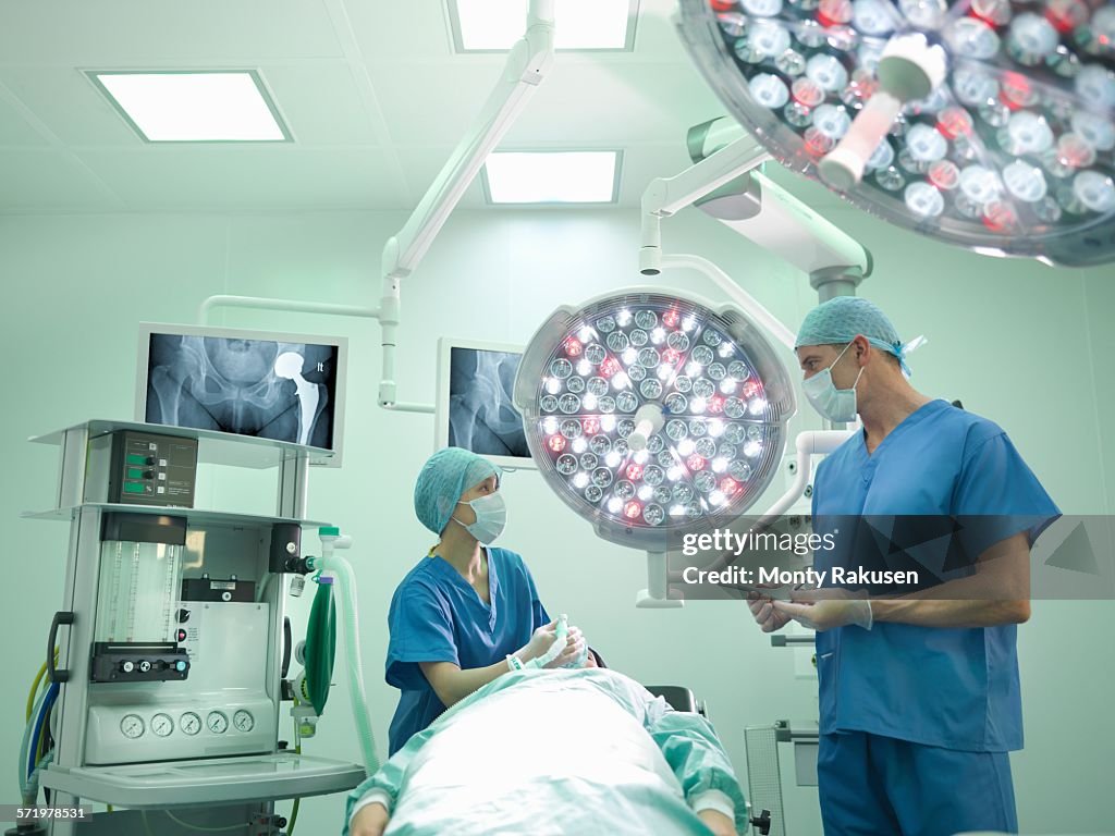 Orthopaedic surgeon and nurse preparing patient for hip surgery in operating theatre
