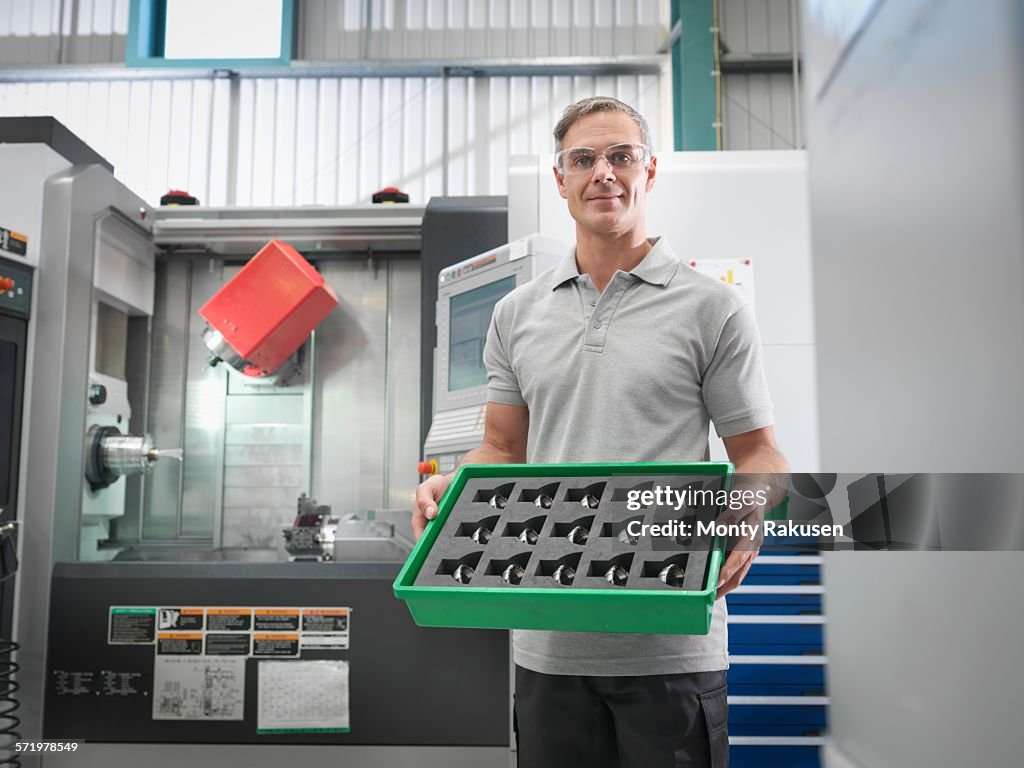 Engineer with CNC lathe holding machined products in orthopaedic factory, portrait