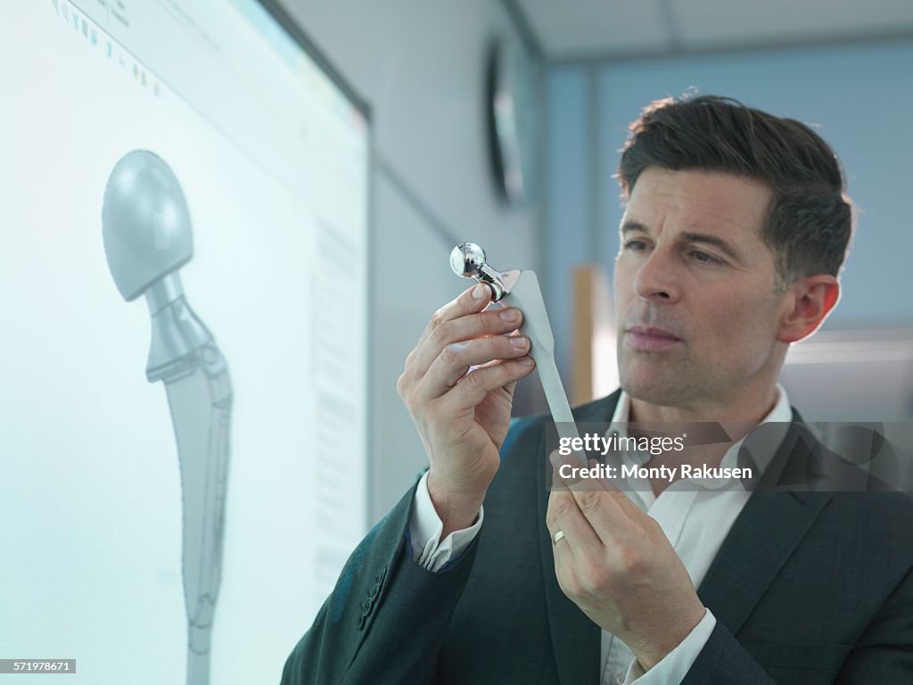 Medical product designer inspecting hip joint model with graphical screen
