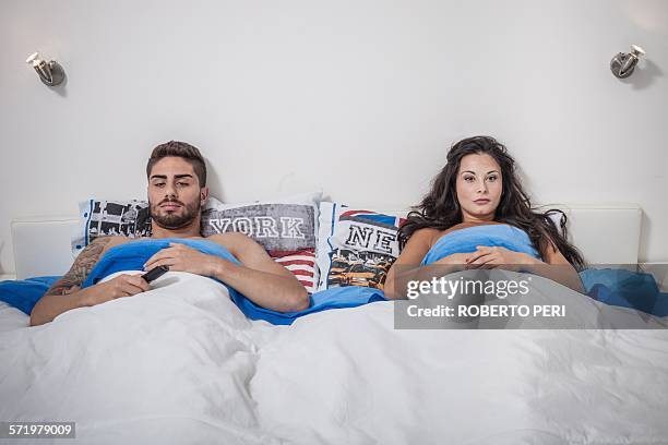 young couple lying in bed sulking - next to stock pictures, royalty-free photos & images