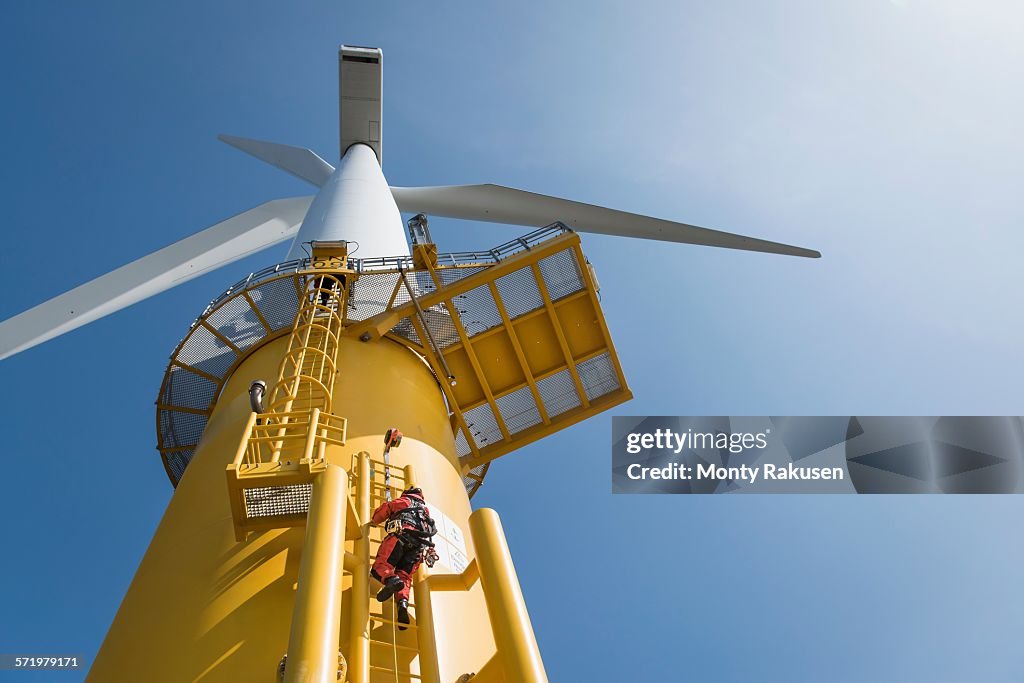 Engineers climbing wind turbine from boat at offshore windfarm, low angle view