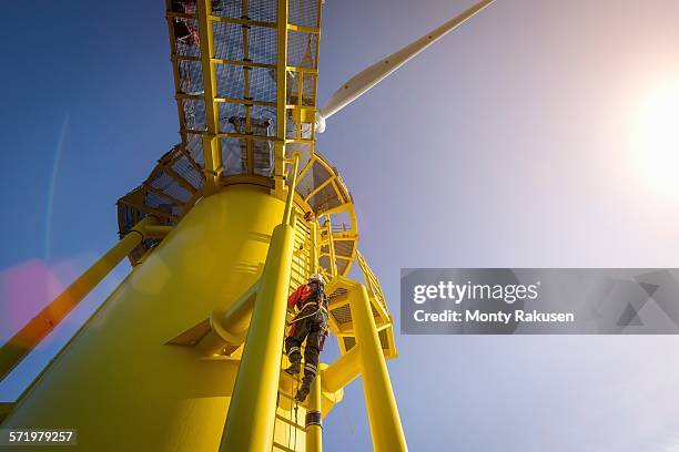 engineers climbing wind turbine from boat at offshore windfarm, low angle view - offshore windfarm stock-fotos und bilder