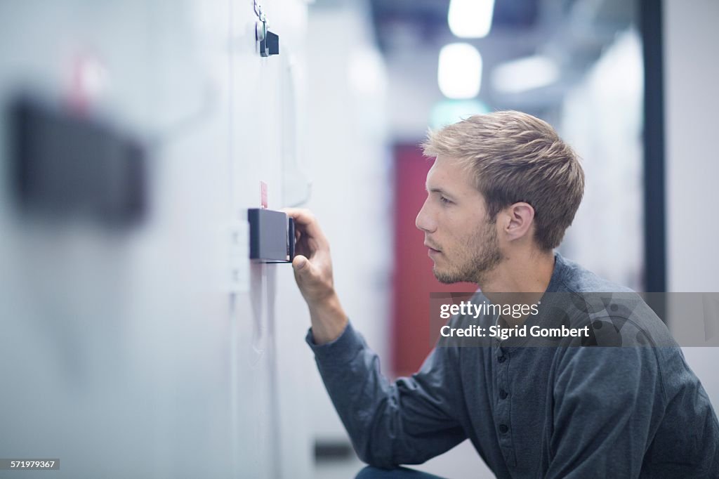 Male technician crouching to turn switch in technical room