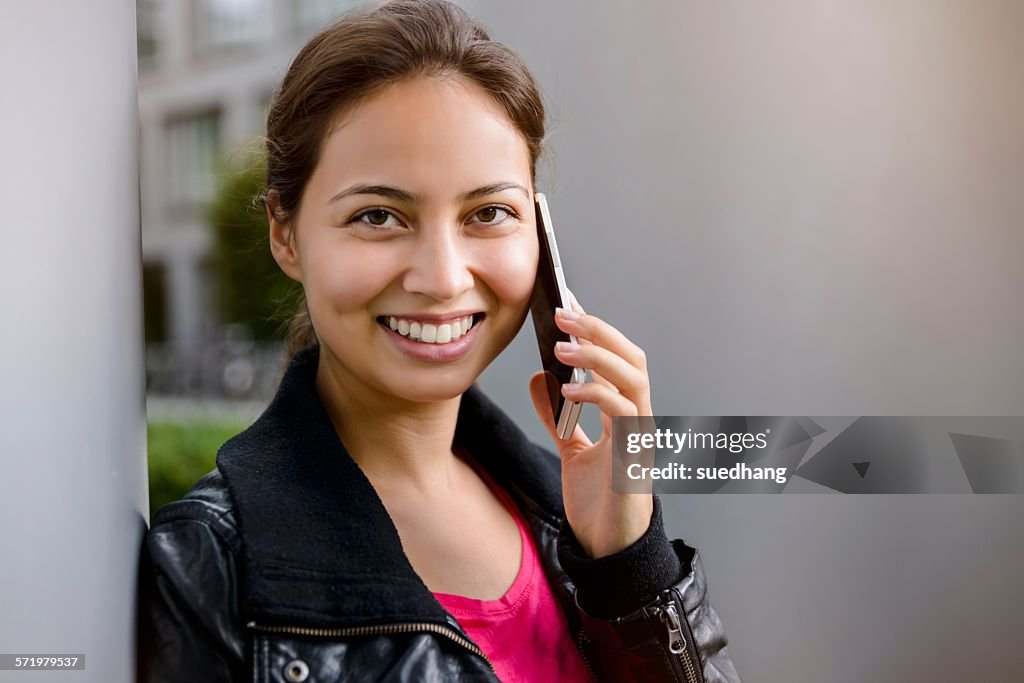 Portrait of young woman leaning against pillar talking on smartphone