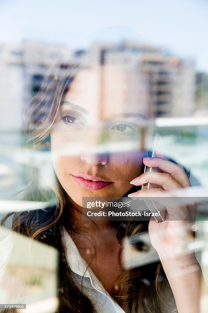 Young woman using smartphone, pensive expression, photographed through glass