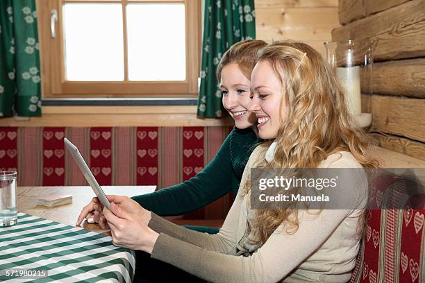 two young women using digital tablet in log cabin - alleen jonge vrouwen stockfoto's en -beelden