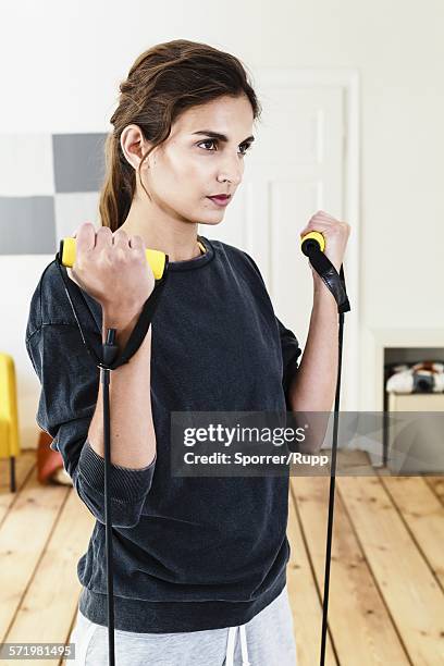 young woman exercising with resistance bands in living room - gym equipment stock-fotos und bilder