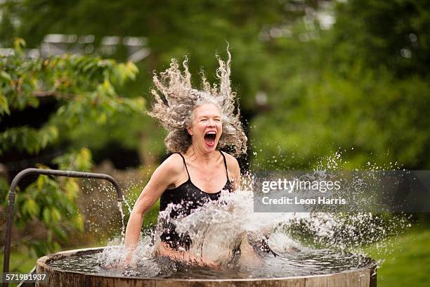 mature woman splashing into fresh cold water tub at eco retreat - frau badewanne stock-fotos und bilder