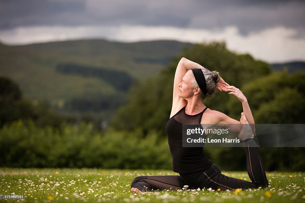 Mature woman doing splits practicing yoga in field