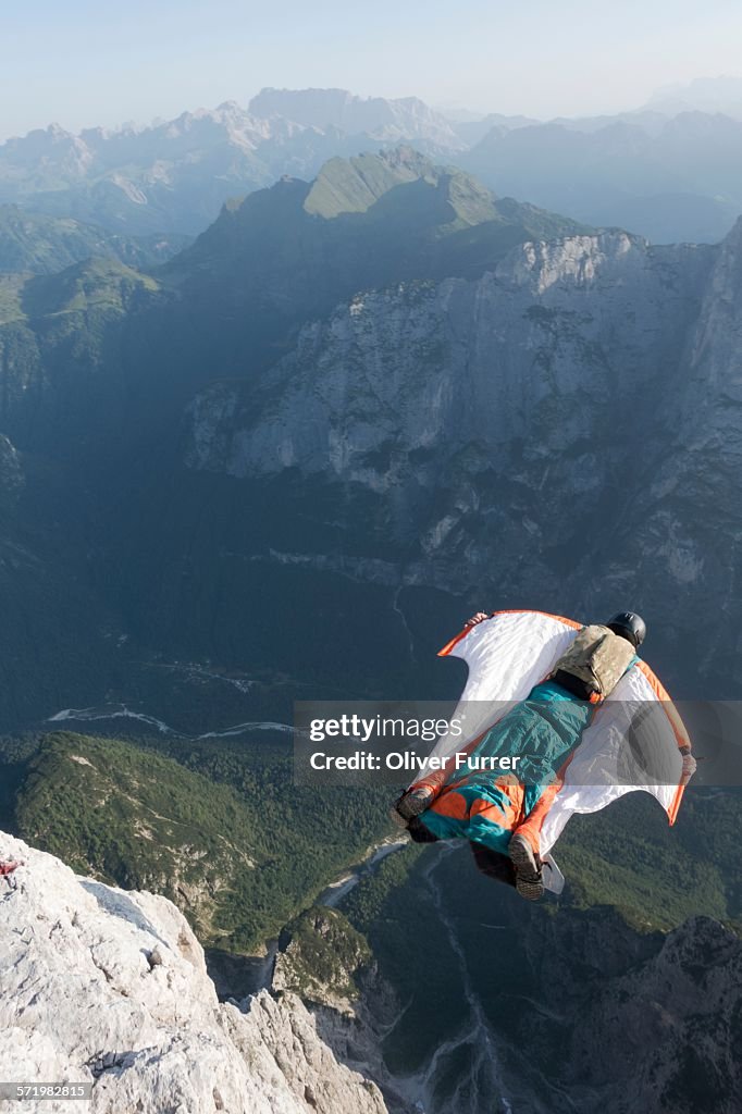 Male BASE jumper wingsuit flying from mountain, Dolomites, Italy