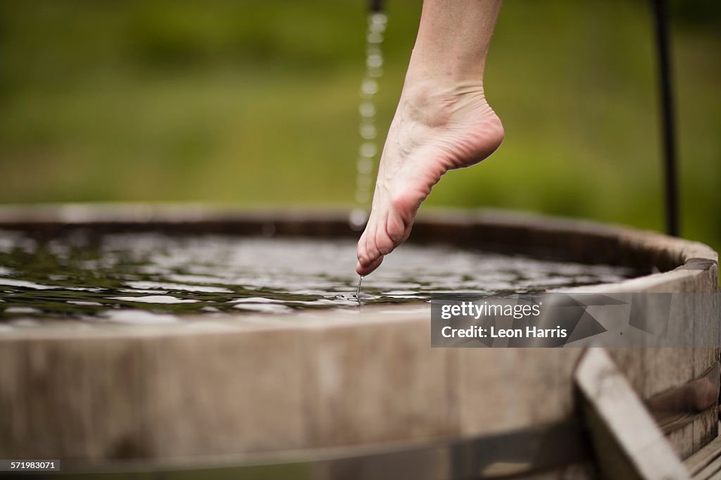 Bare foot of mature woman stepping into fresh cold water tub at eco retreat