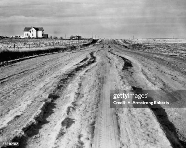 1940s: Heavily rutted dirt country road near Dickinson, North Dakota, farm house on the horizon.