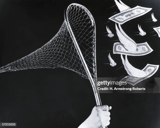 1940s: Man holding butterfly fishing net, trying to catch flying currency, dollar bills and coins with wings.