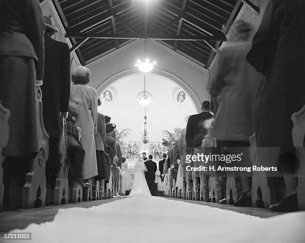 1960s: Bride and groom partaking in wedding ceremony in church, rear view.