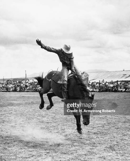 1960s: Rodeo cowboy riding bucking bronco horse in arena.