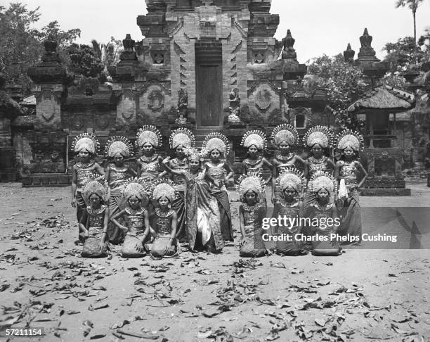 Group of sixteen female dancers posing in two rows in front of Balinese temple, Indonesia.