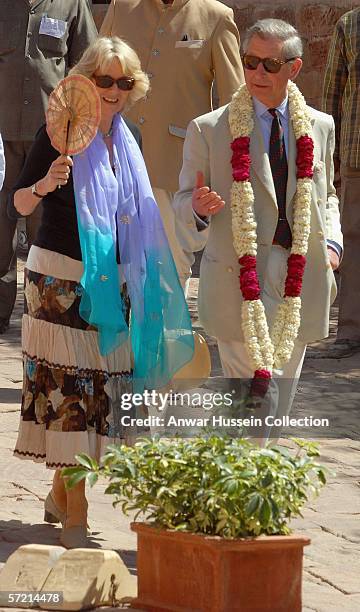 Camilla, Duchess of Cornwall fans herself in the heat and Prince Charles, Prince of Wales wears a garland as they visit the arts and craft market at...