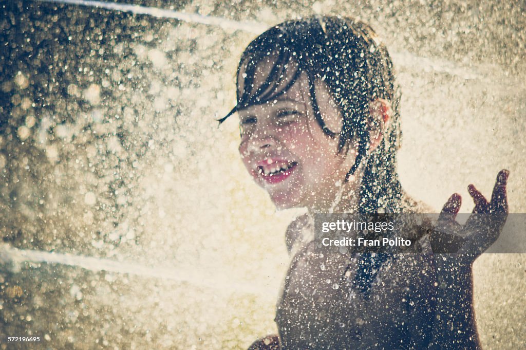 Boy playing in a sprinkler surrounded by water