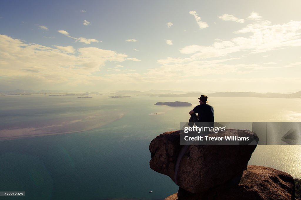 A man sitting on a mountain wtching the sun set