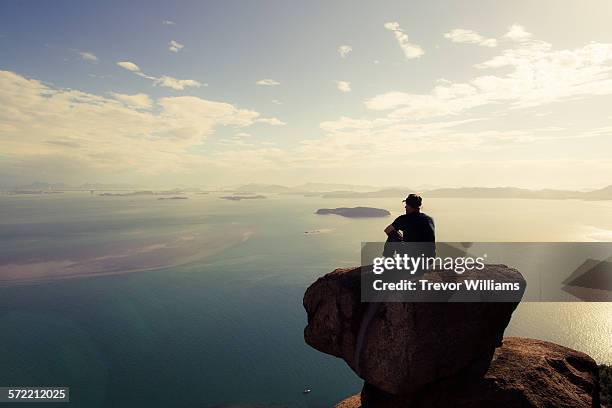 a man sitting on a mountain wtching the sun set - sitting on a cloud foto e immagini stock