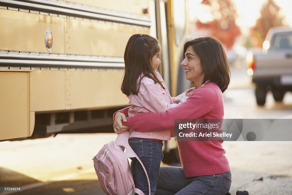 Mother saying goodbye to daughter at school bus