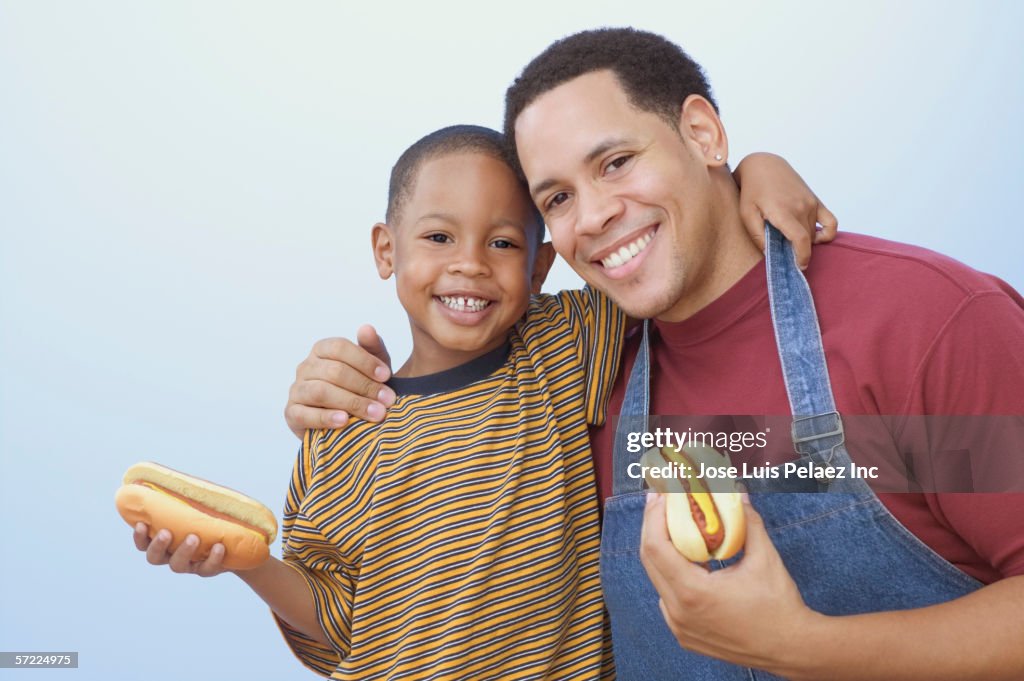 Father and son hugging while holding hot dogs