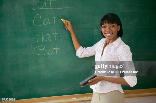 portrait of female teacher pointing to words on chalk board - teacher board stock pictures, royalty-free photos & images