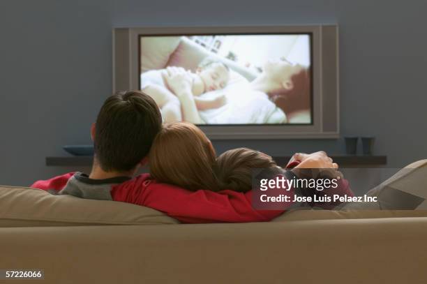 rear view of family on couch watching television - family watching tv from behind stock pictures, royalty-free photos & images