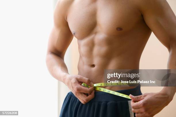 mid section of man measuring his waist with measuring tape - measuring tape stockfoto's en -beelden