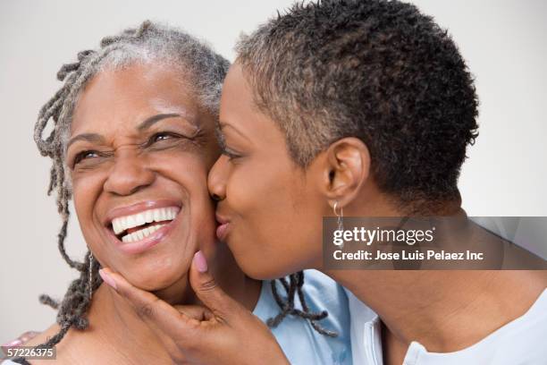 close up of grown daughter kissing mother on cheek - studio kiss stock pictures, royalty-free photos & images