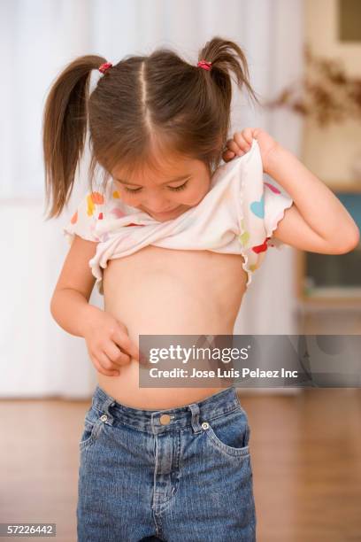 young girl lifting shirt while pointing at belly button - kids belly stock pictures, royalty-free photos & images