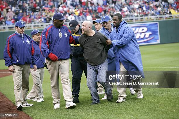 Fan is escorted off the field at the game of the Philadelphia Phillies against the St. Louis Cardinals during the Phillies' Home Opener on April 3,...