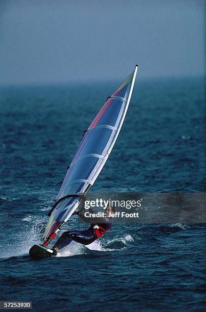 man glides the waves while windsurfing. - wind surfing stock pictures, royalty-free photos & images