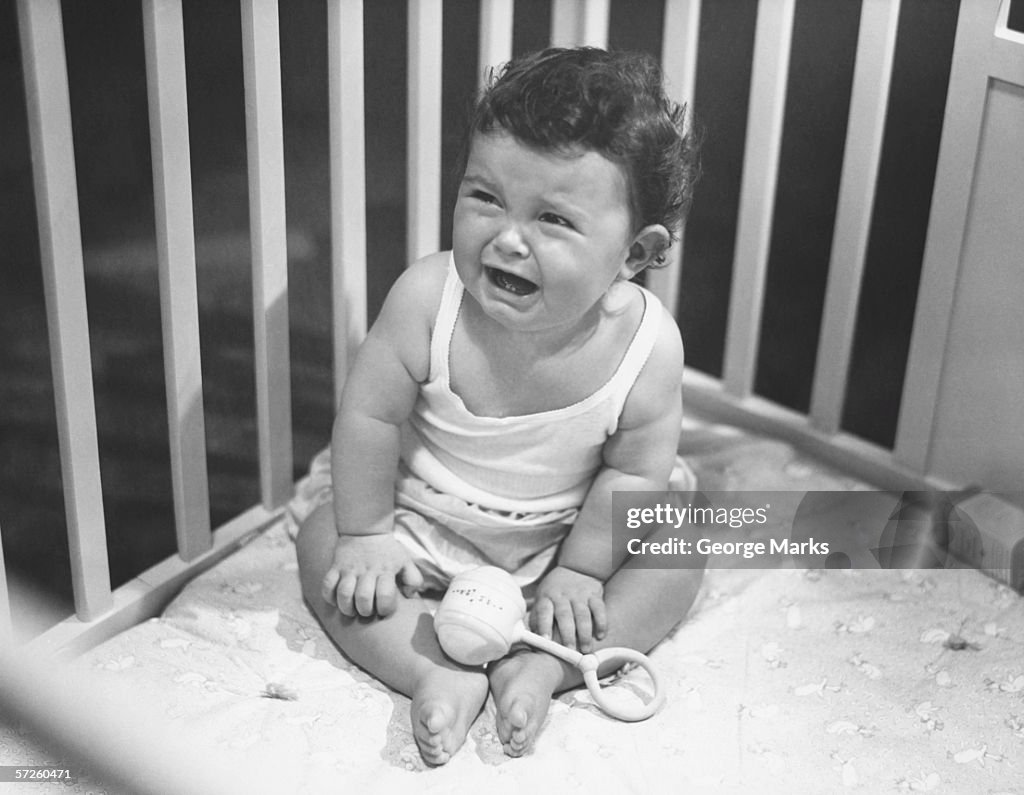 Baby girl (6-12 months) crying in playpen, (B&W), (Elevated view)