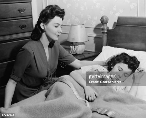 mother looking at sleeping daughter (8-9), (b&w) - 1940s bedroom stock pictures, royalty-free photos & images