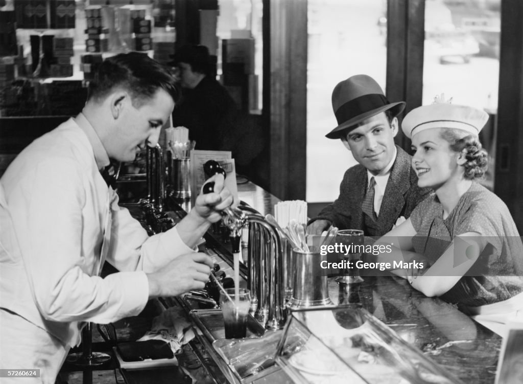 Bartender pouring beer for young couple in bar, (B&W)