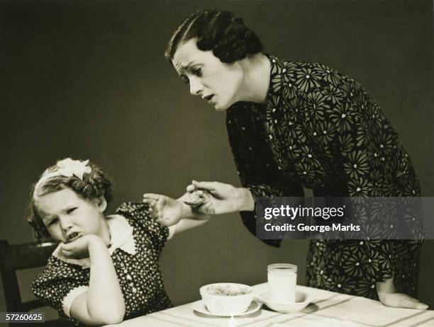 mother trying to make daughter (4-5) finish food at table, (b&w) - vintage mother and child stock pictures, royalty-free photos & images