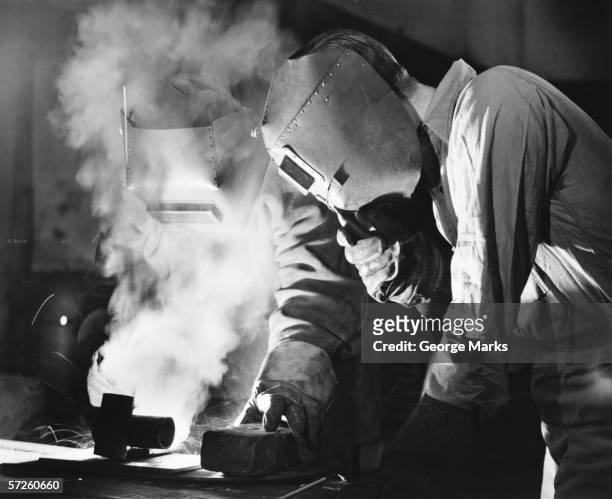 two men welding, holding protective masks, (b&w) - 20th century stock pictures, royalty-free photos & images