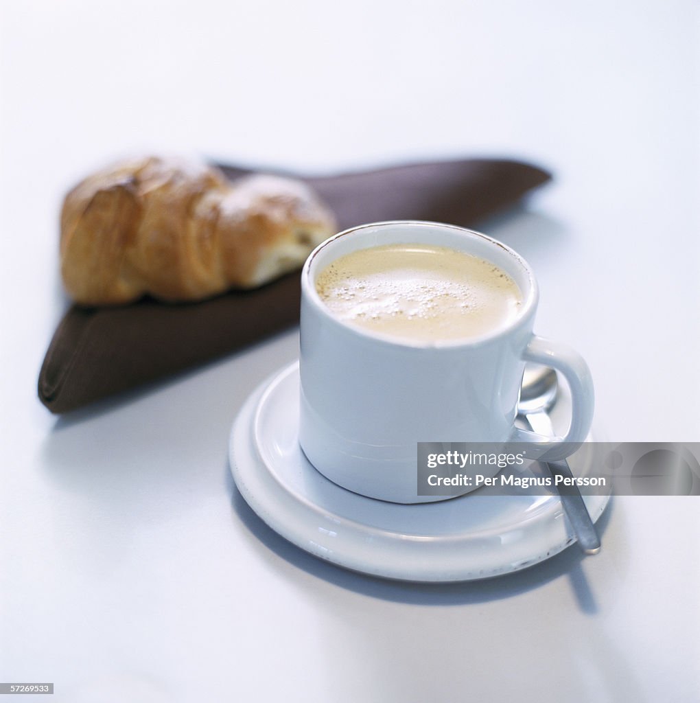 A cup of coffee and a croissant in the background.