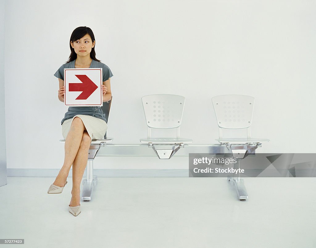 Portrait of a young woman sitting on a chair holding an arrow sign