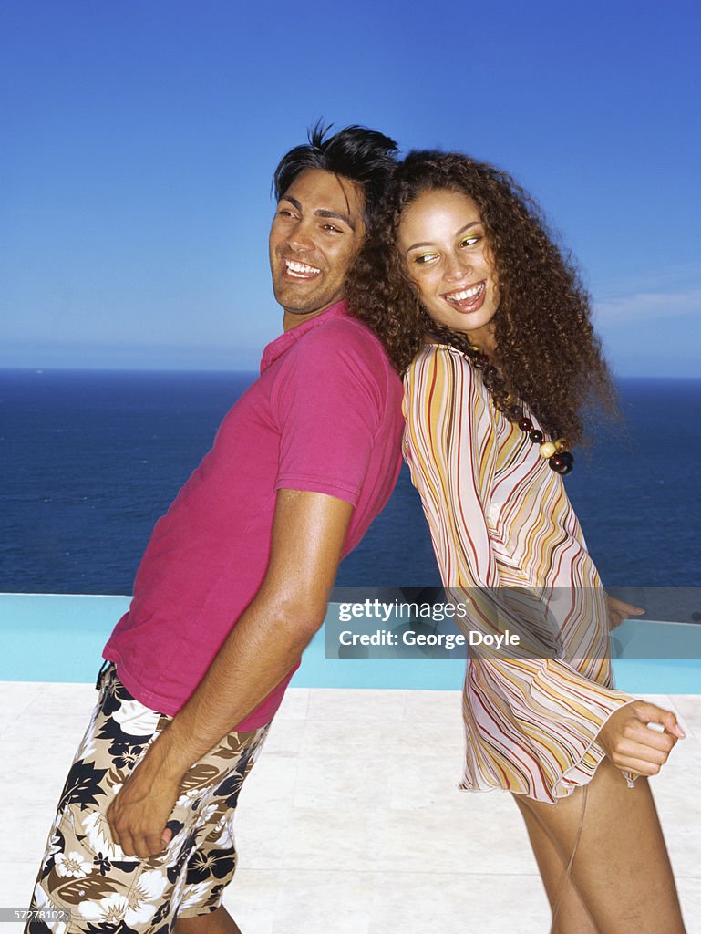 Side profile of a young couple smiling and standing back to back