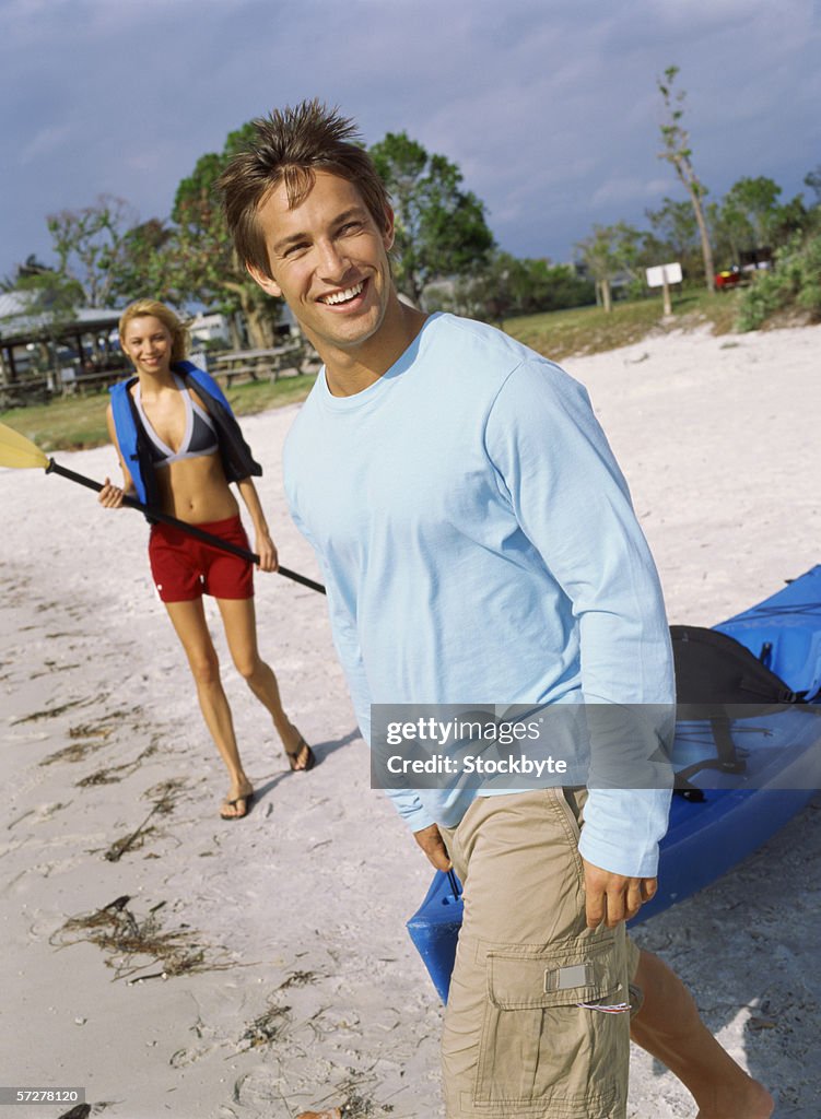 Side profile of a young man on the beach, pulling a canoe