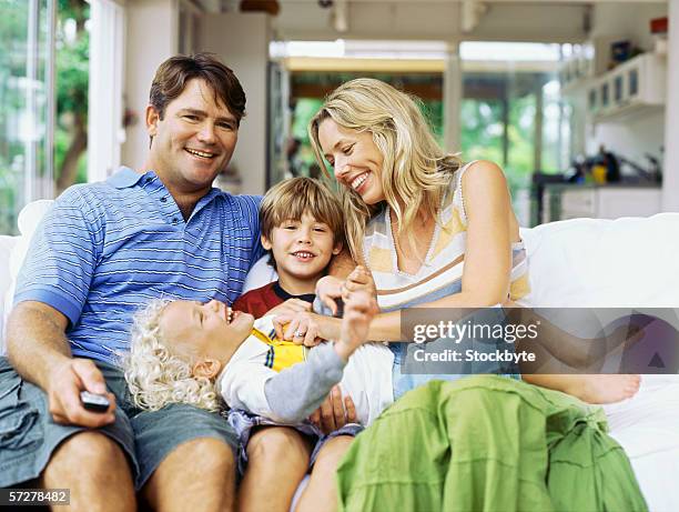 mid adult woman tickling her daughter with her husband and son sitting beside her - front view portrait of four children sitting on rock stock-fotos und bilder