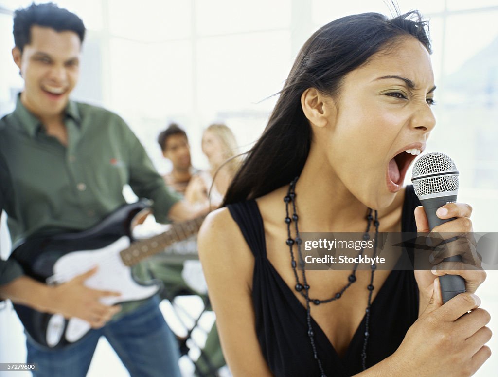 Close-up of a young woman singing with a young man playing guitar behind her