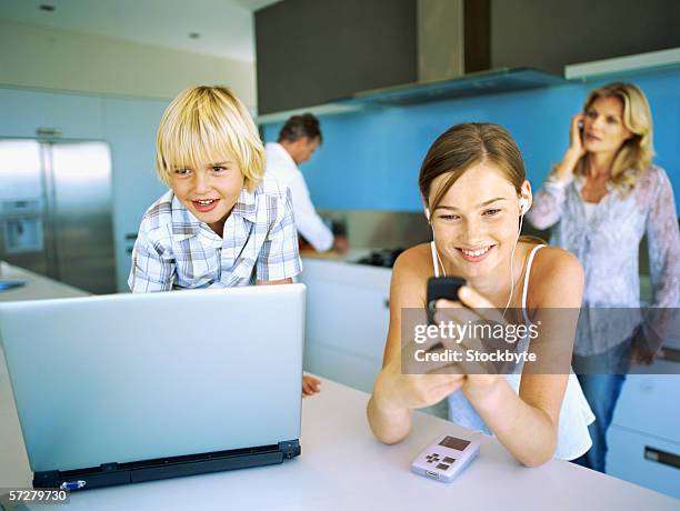 close-up of two children in front of a laptop with their parents standing behind them - brother sister stock pictures, royalty-free photos & images