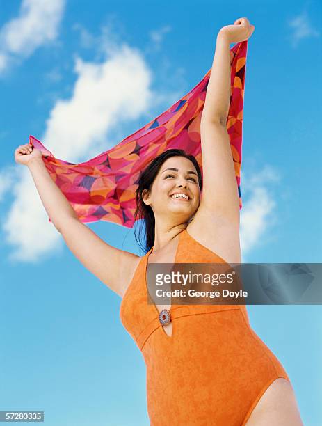low angle view of a young woman standing with her arms raised, holding a sarong - dicke frauen am strand stock-fotos und bilder