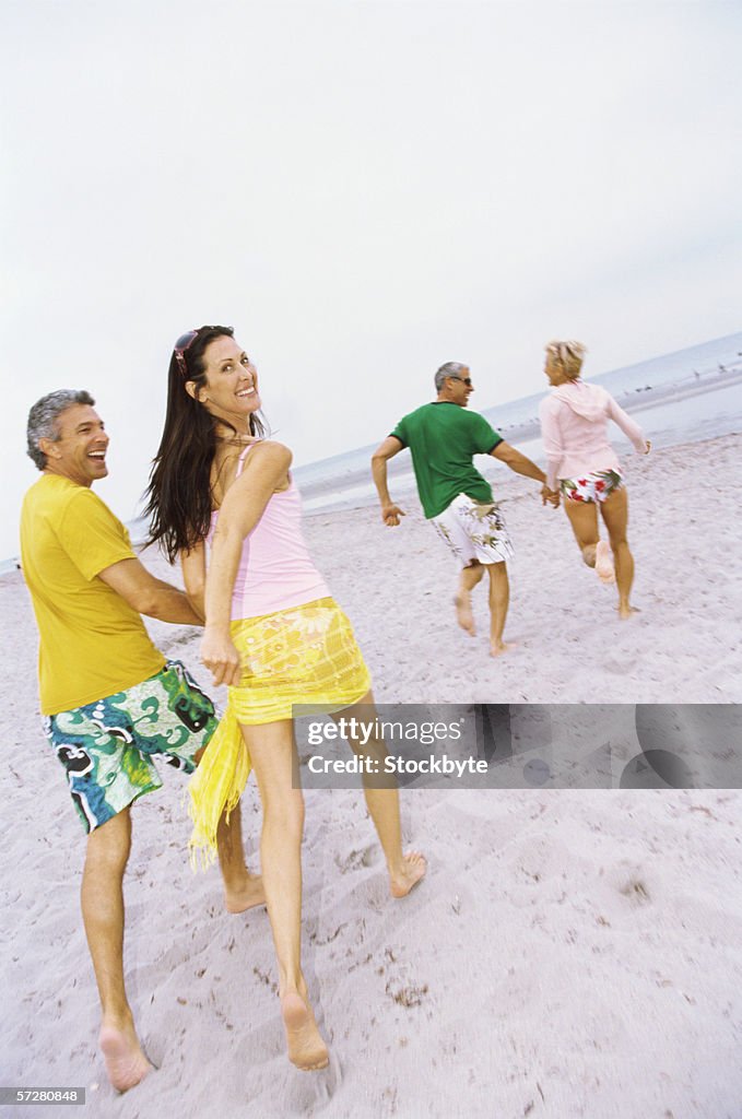 Rear view of two mature couples running on the beach