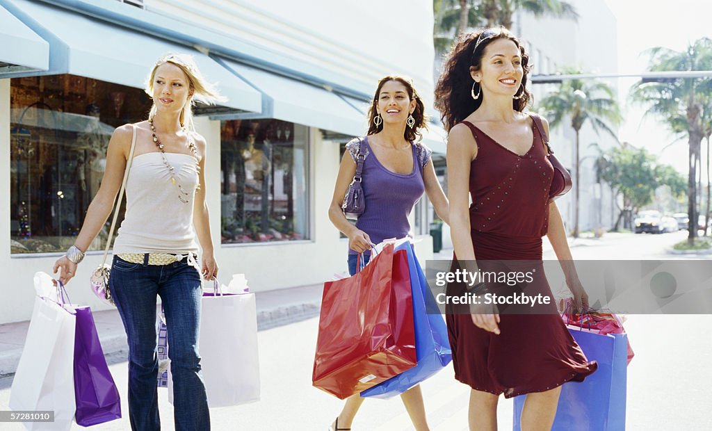 Side view of three young women walking and holding shopping bags