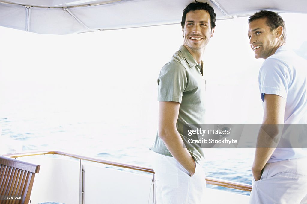 Two young men standing on the deck of a motorboat and looking away